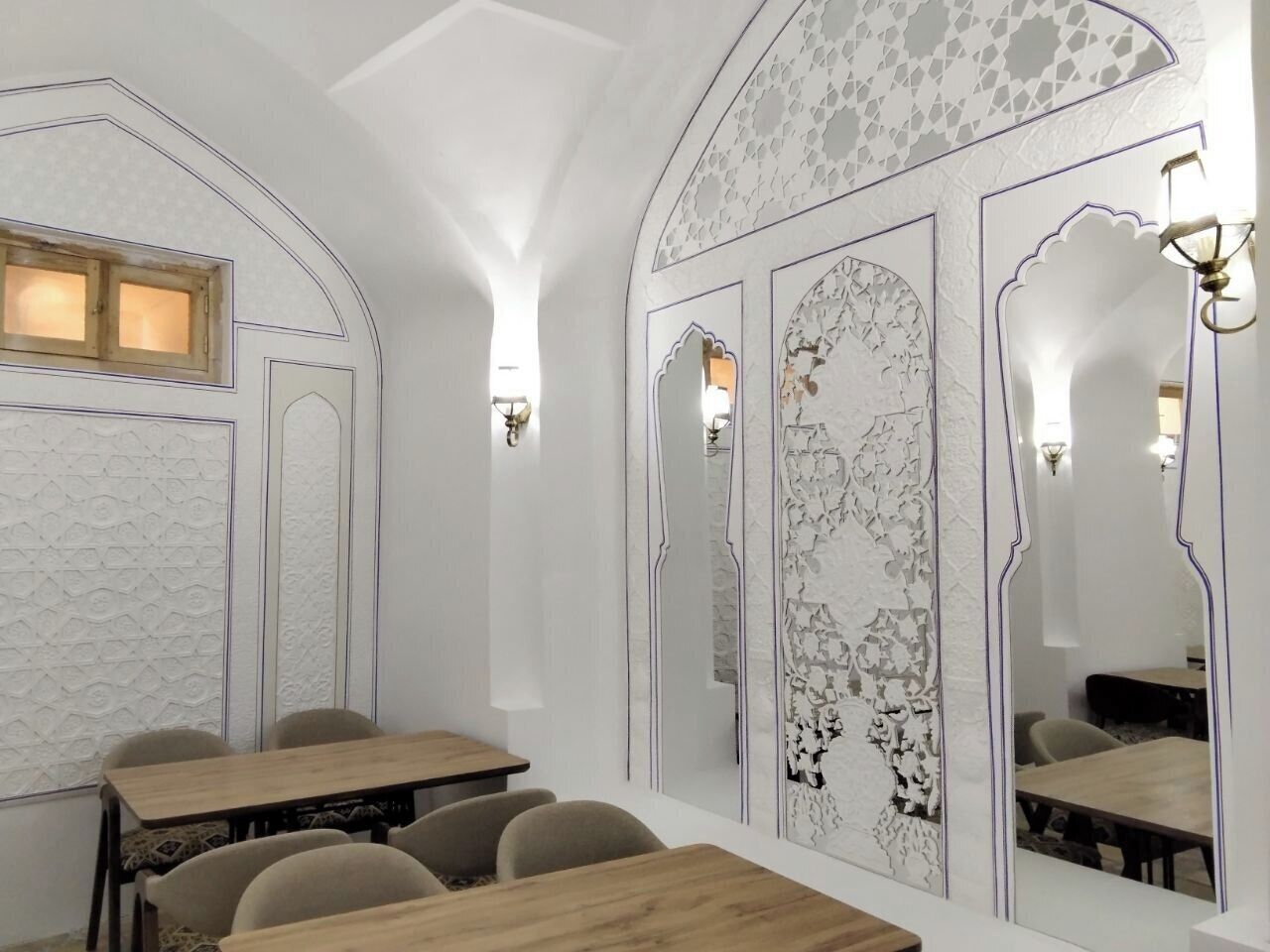 Un espace repas doté d’un plafond haut, de murs à motifs et d’un grand miroir.
