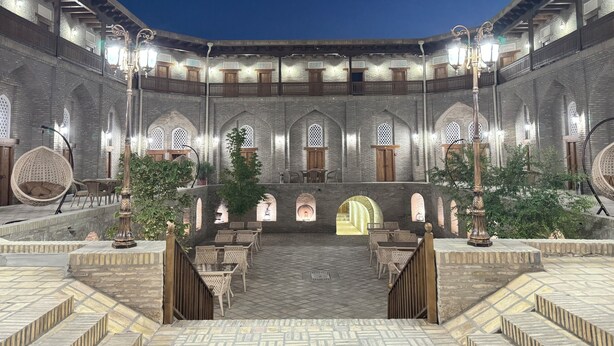 A courtyard with a tiled floor, wooden furniture, and arched doorways. - Hotel Caravansaray Rashid in Bukhara  (Bukhara)