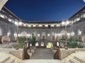 A courtyard with a tiled floor, wooden furniture, and arched doorways. - Hotel Caravansaray Rashid in Bukhara (Bukhara)