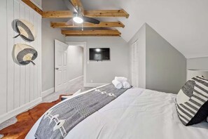 A bedroom with a bed, a ceiling fan, a mounted TV, and a door leading to another room.