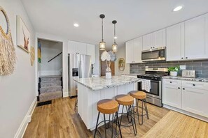 A modern kitchen with white cabinets, a granite island with bar stools, stainless steel appliances, and pendant lighting.