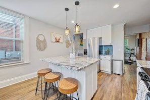 A modern kitchen with a marble island, bar stools, stainless steel appliances, and pendant lighting.
