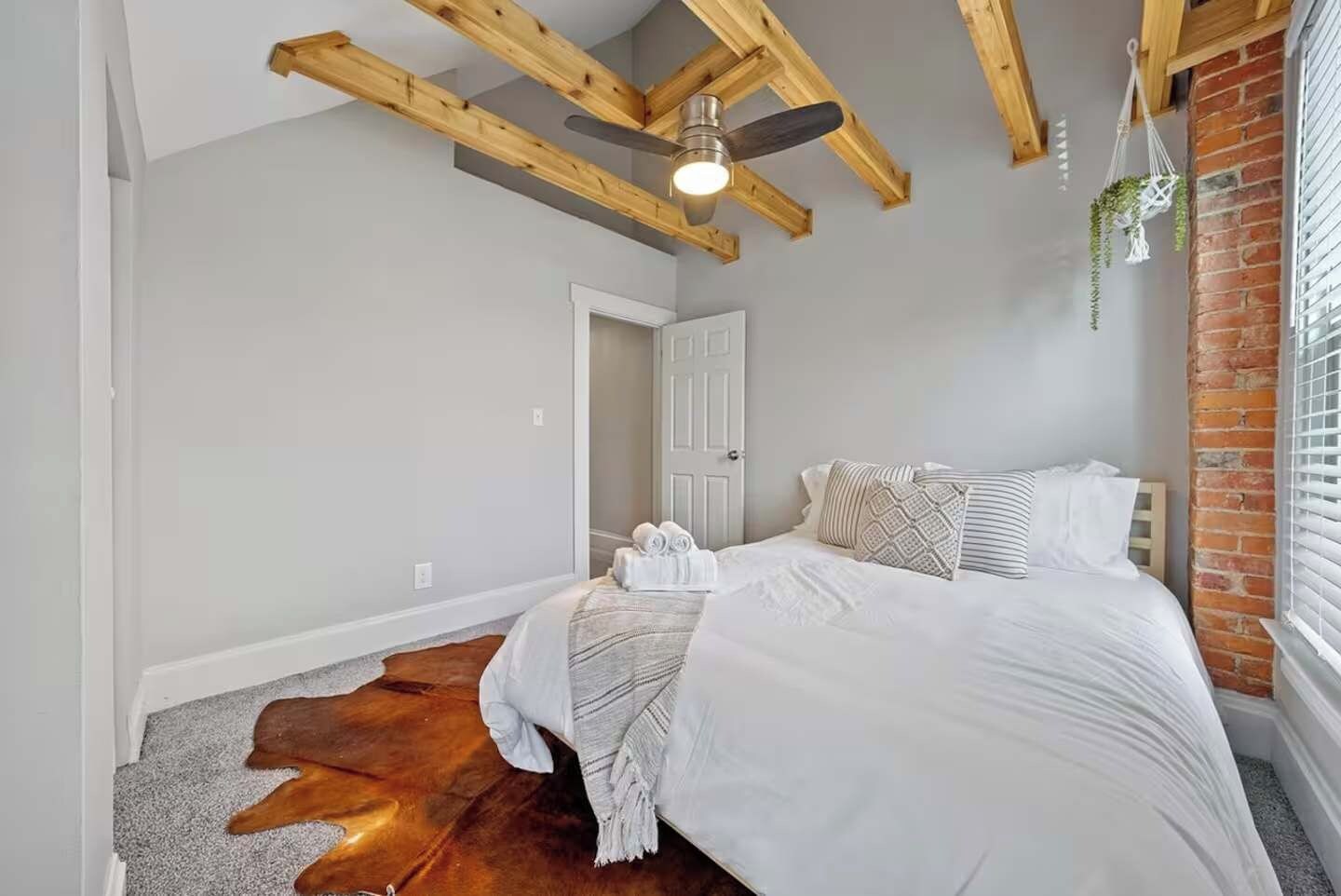 A bedroom with a bed, a ceiling fan, a door, and a brick wall.