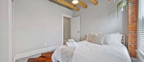 A bedroom with a bed, a ceiling fan, a door, and a brick wall.