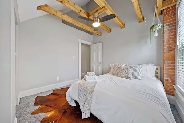 A bedroom with a bed, a ceiling fan, a door, and a brick wall.