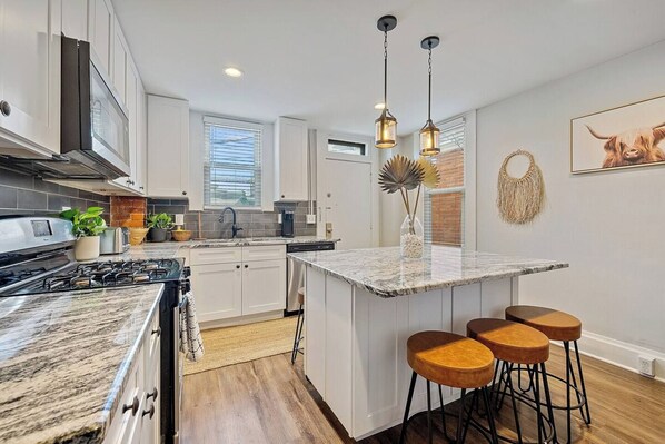 A modern kitchen with white cabinetry, a granite countertop, a gas stove, and a central island with bar stools.