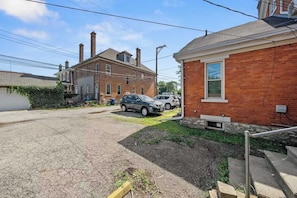 A residential street with brick houses, parked cars, and a visible driveway.
