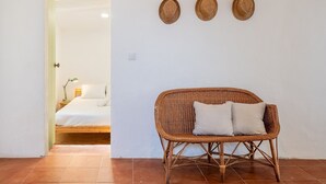 Une chaise en osier avec des coussins, un lit avec une literie blanche et trois éléments de décoration murale en fibres tressées.