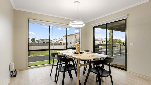 Comedor con una mesa dispuesta para cuatro, ventanas amplias y vista a un barrio residencial.