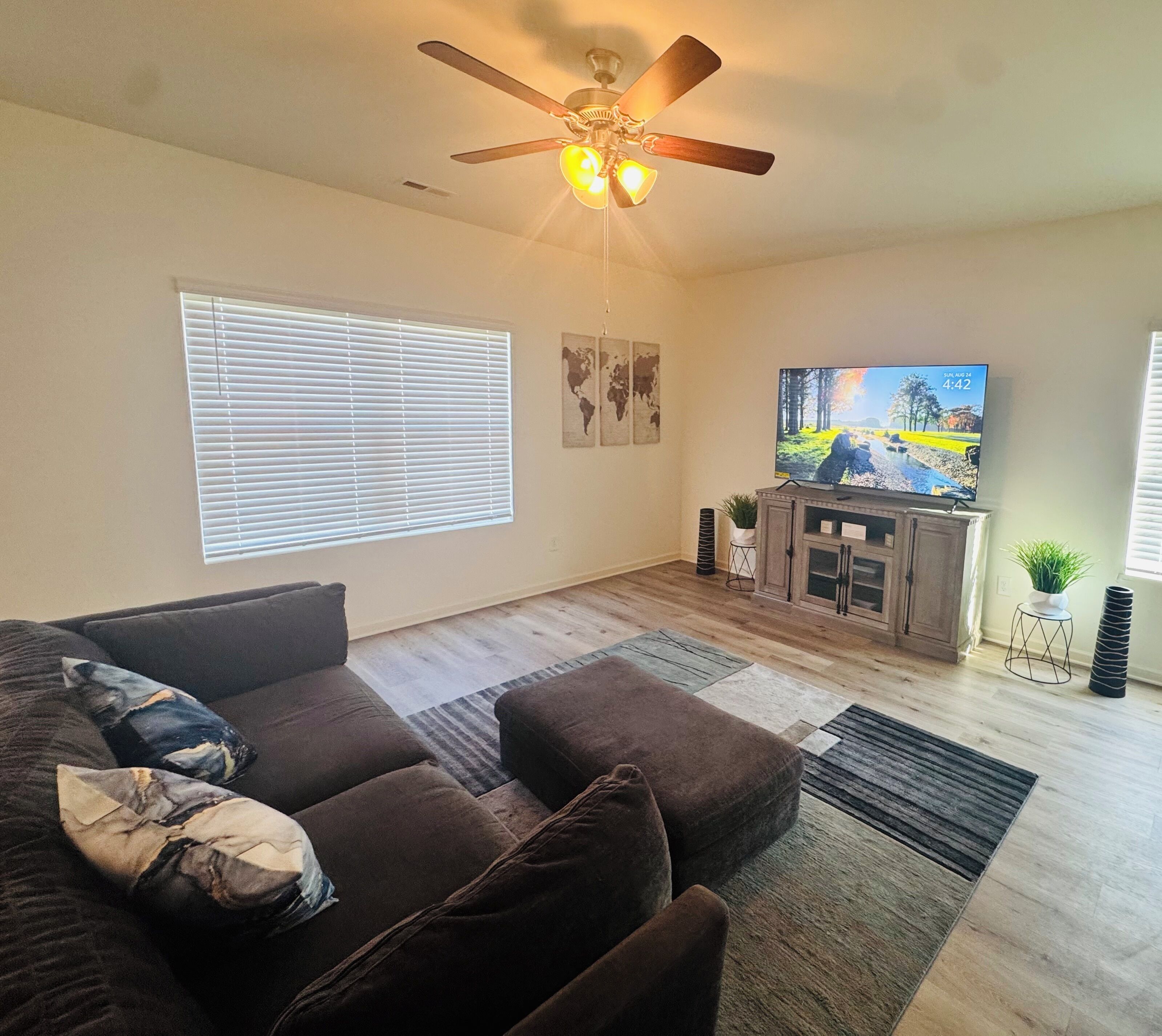 A living room with a dark brown sofa, a ceiling fan, a flat-screen TV, and a wooden floor.