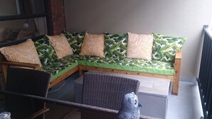 Un sofá de esquina con funda estampada de hojas y cojines a juego, una silla de mimbre y una estatua decorativa de un búho.