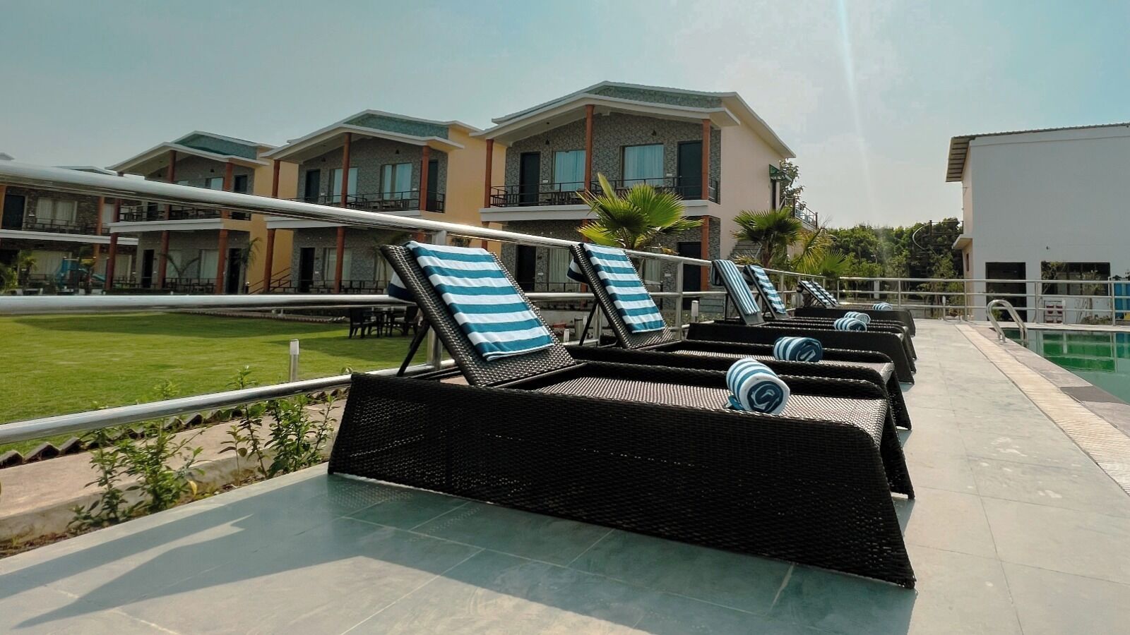 Outdoor lounge chairs with striped cushions, a swimming pool, and modern buildings in the background.