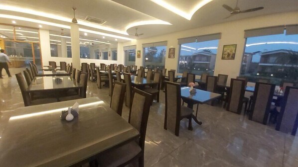 Un comedor moderno con varias mesas y sillas, ventanas amplias con vistas a la ciudad y ventiladores de techo.