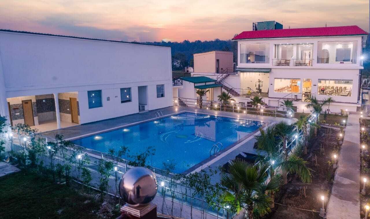 A modern building with a swimming pool, a covered area, and a red-roofed structure.