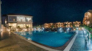 Vista nocturna de un hotel con piscina, varias habitaciones de huéspedes y un área exterior bien iluminada.