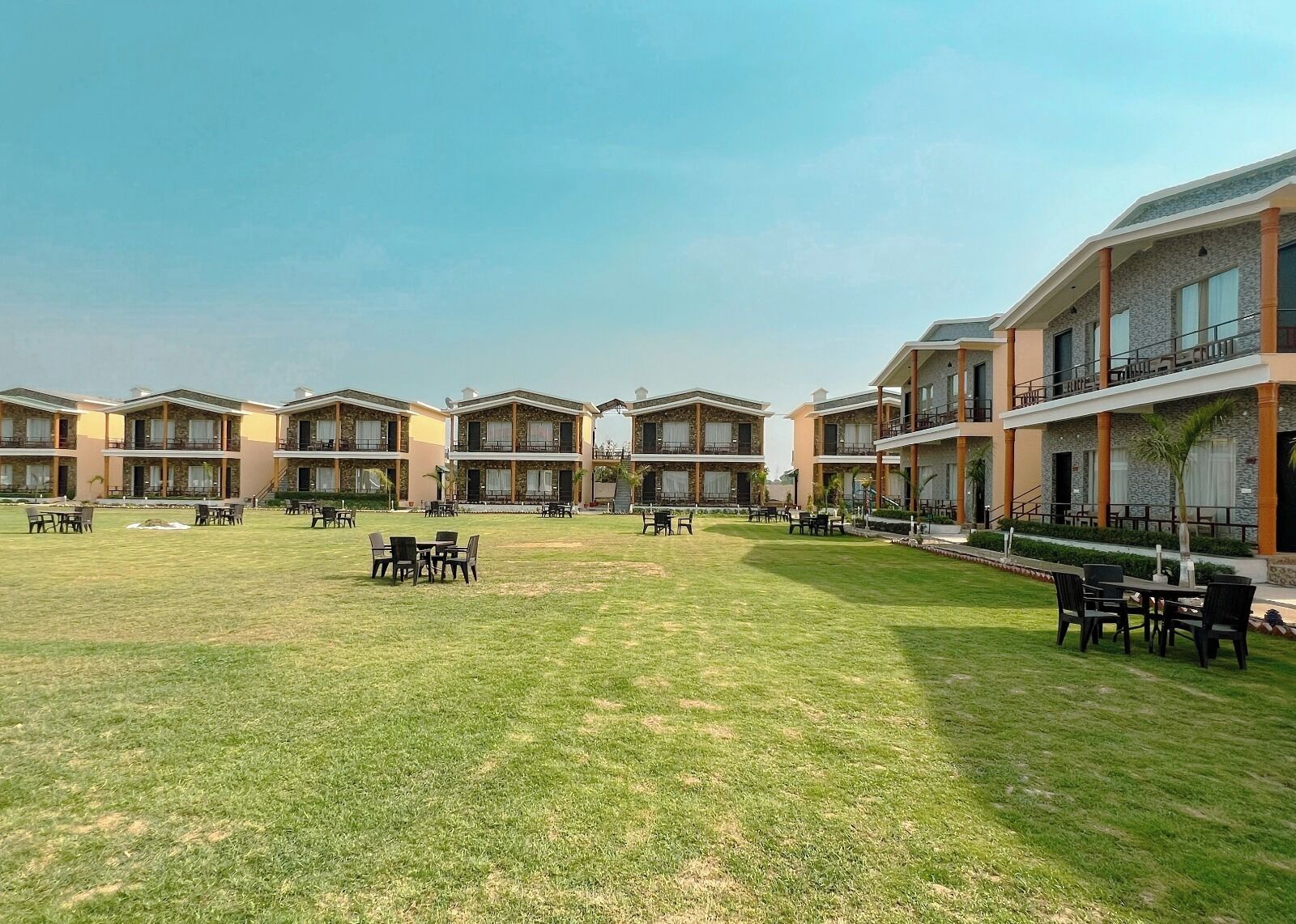 A hotel courtyard with multiple buildings, outdoor seating areas, and a well-maintained lawn.