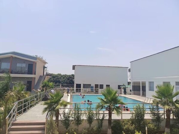 Uma área de piscina com escadas de acesso, cercada por palmeiras e edifícios modernos.