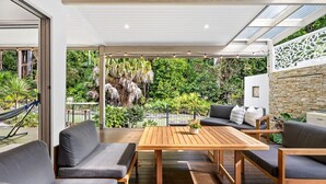 An outdoor patio with wooden furniture, a hammock, and lush greenery in the background. - Spacious 3-Bed Home with Patio Near Beach (Alexandra Headland)