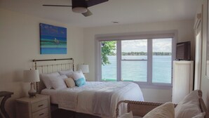 A bedroom with a large window, a bed with white bedding, a nightstand with a lamp, and a painting on the wall. - New renovation Moon River (Marine City)