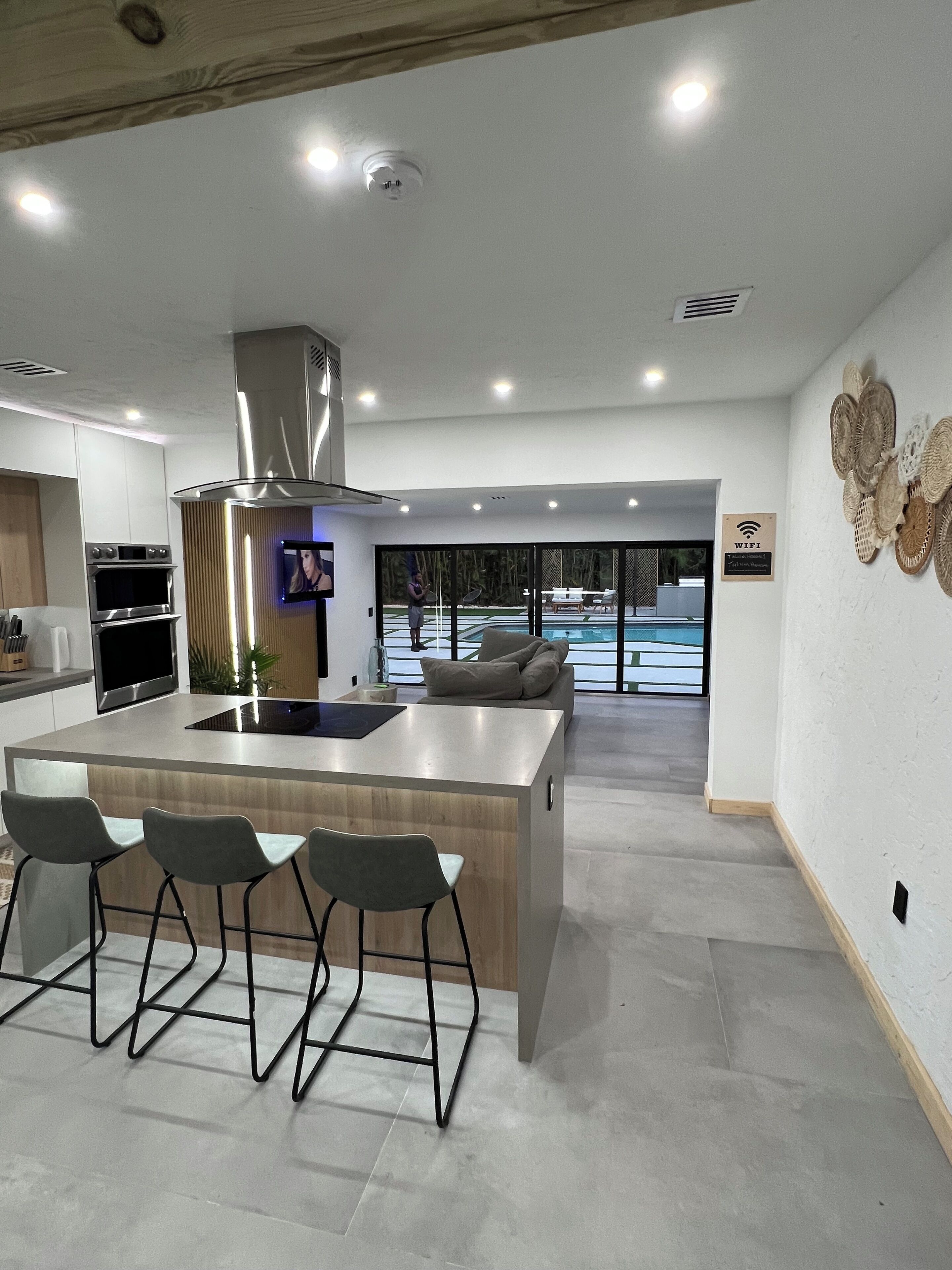 Una cocina moderna con una isla central, taburetes de bar y vistas a una piscina exterior.