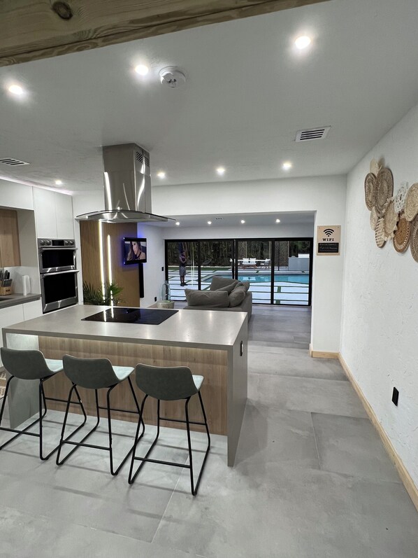 Una cocina moderna con una isla central, taburetes de bar y vistas a una piscina exterior.