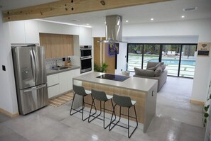Una cocina moderna con una isla central, electrodomésticos de acero inoxidable y vistas a una piscina.
