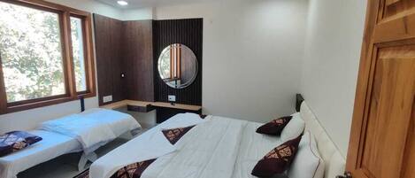 A hotel room with two single beds, a ceiling fan, a large mirror, and a view of trees through the window.