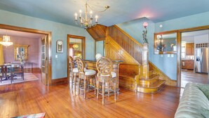 A spacious living room with a wooden staircase, a dining area with chairs, and a chandelier. - Fire Pits, Views & Yard: Luxe Mt Horeb Getaway! (Mt Horeb)