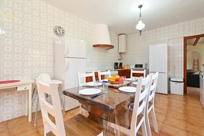 A dining area with a wooden table, white chairs, and a fruit bowl. There is a white refrigerator, a white oven, and a white washing machine in the background. - Jalna 6 pax - Javea, Costa Blanca (Javea)