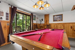Ein Billardtisch mit roter Spielvliesbahn, Holzrahmen und einem Fenster mit Vorhängen.