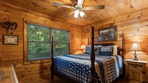 A wooden cabin bedroom with a four-poster bed, a ceiling fan, and a window with blinds.