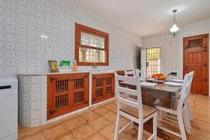 A kitchen with a tiled backsplash, wooden cabinets, a dining table with chairs, and a window with a view of the outside.