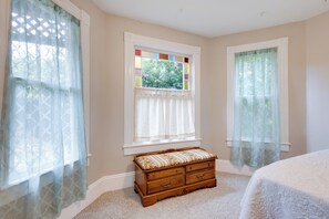 Een slaapkamer met een houten dressoir, een raam met een glas-in-lood ontwerp en lichte gordijnen.
