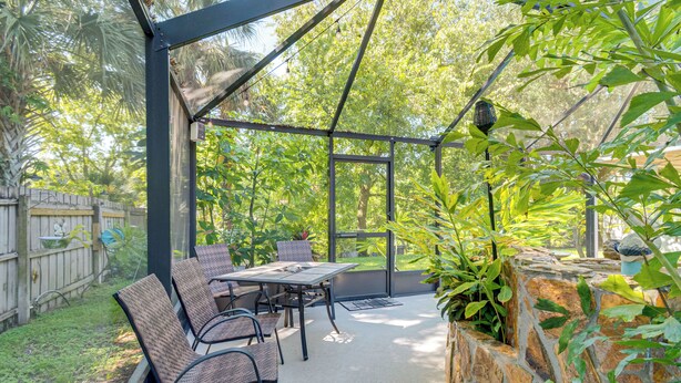 An outdoor patio with a table and chairs, surrounded by greenery and a stone wall. - Private Backyard Oasis: Cocoa Family Home! (Cocoa)