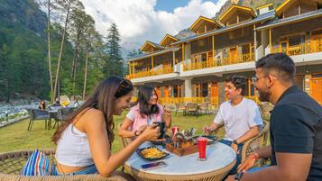 Un grupo de personas cenando al aire libre en un restaurante con montañas al fondo.