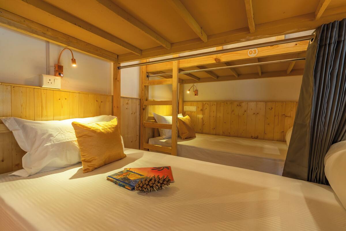 A wooden cabin room with bunk beds, a reading lamp, and a window with curtains.