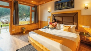 Een slaapkamer met houten meubels, een groot bed, een schilderij boven het bed en uitzicht op een rotsachtig landschap door het raam.