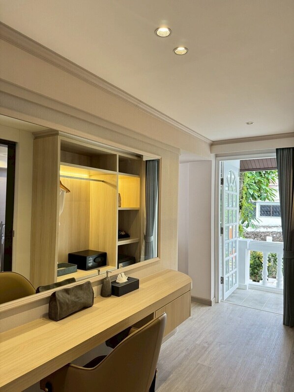 A hotel room with a wooden desk, a mirror, a wardrobe, and a view of the outside. - Villa Atchara (Patong)