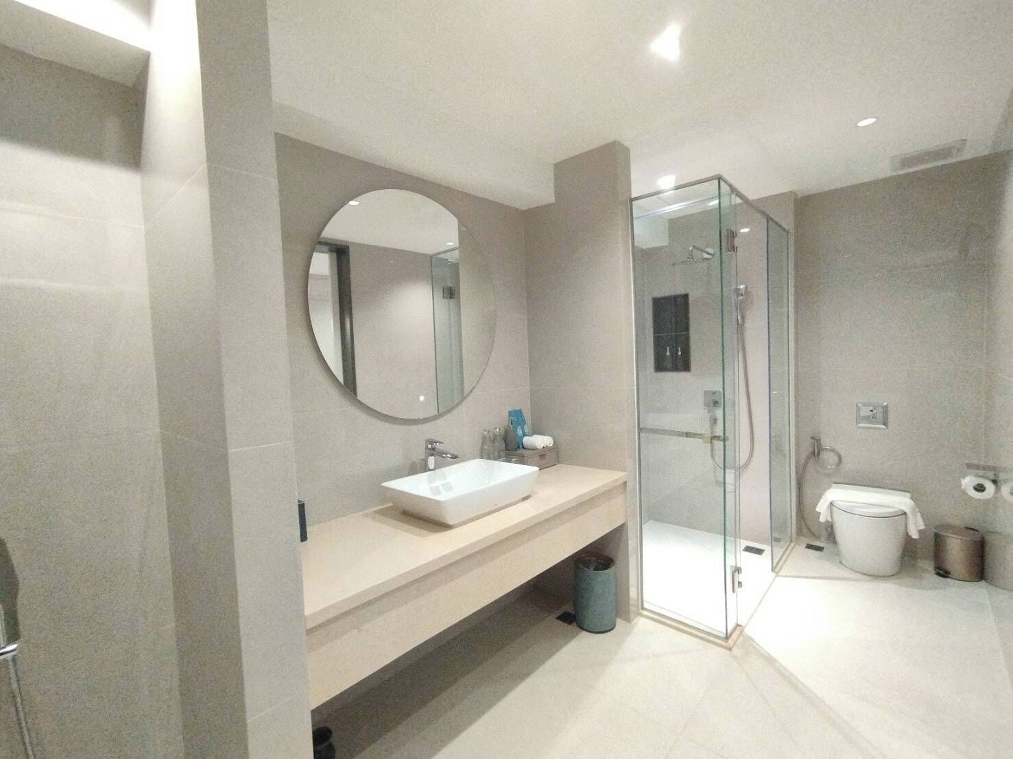 A modern bathroom with a glass-enclosed shower, a round mirror, and a beige vanity.