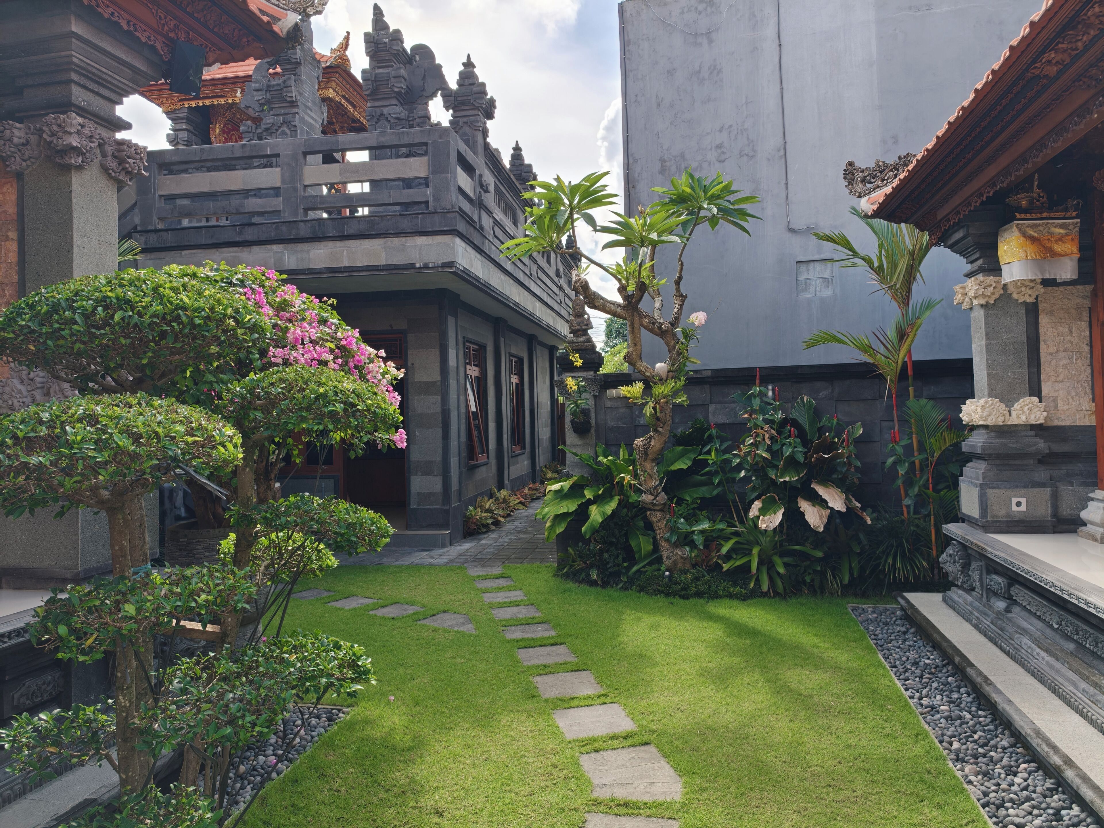 A courtyard with a stone pathway, lush greenery, and traditional architecture.