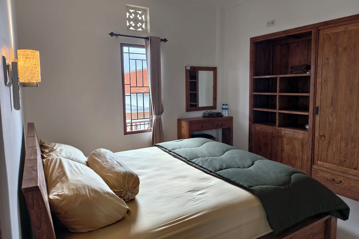 A bedroom with a bed, a wooden wardrobe, a desk, and a window with curtains.