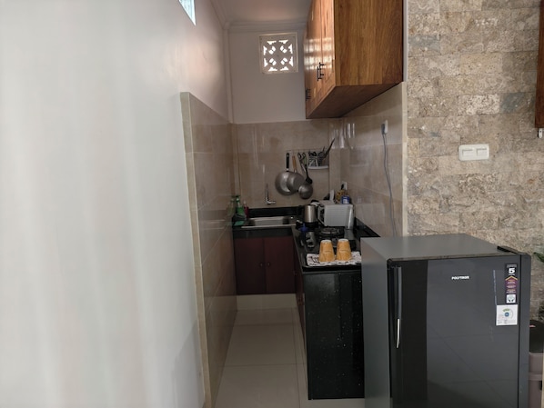A compact kitchen with a refrigerator, stove, sink, and wooden cabinets. - Ayuna Guest House (Celuk)