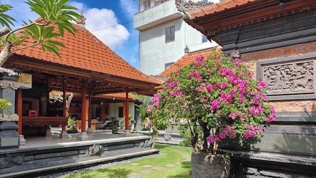 A traditional Balinese courtyard with a tiled roof, stone pathway, and a central flower arrangement. - Ayuna Guest House (Celuk)