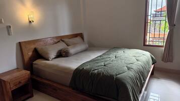 Un dormitorio con cabecera de madera, colcha verde, mesita de noche y ventana con cortinas.