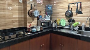 A modern kitchen with wooden cabinetry, a black countertop, and various kitchen utensils and appliances. - Ayuna Guest House (Celuk)