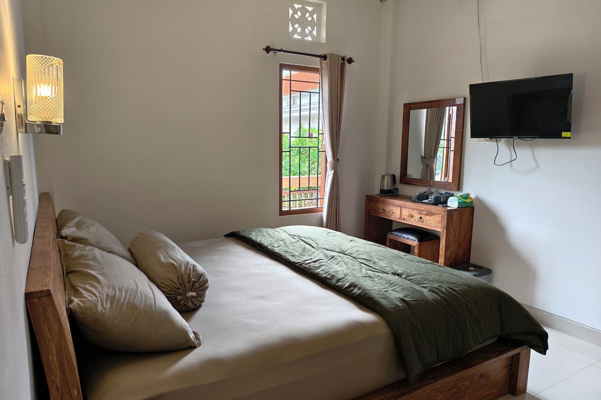 A bedroom with a bed, a wooden dresser, a mirror, a television, and a window with curtains.