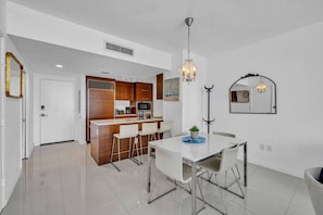 A modern kitchen with a bar area, a dining table with chairs, and a chandelier.