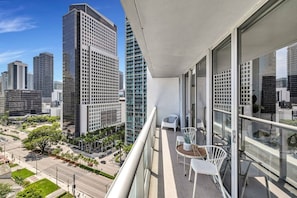 A balcony with a table and chairs, overlooking a cityscape with tall buildings.