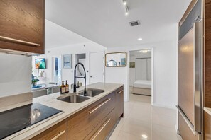 Una cocina moderna con una isla grande, electrodomésticos de acero inoxidable, armarios de madera y vistas al dormitorio.