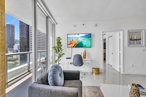 A modern living room with a large window, a flat-screen TV, and a view of the cityscape.